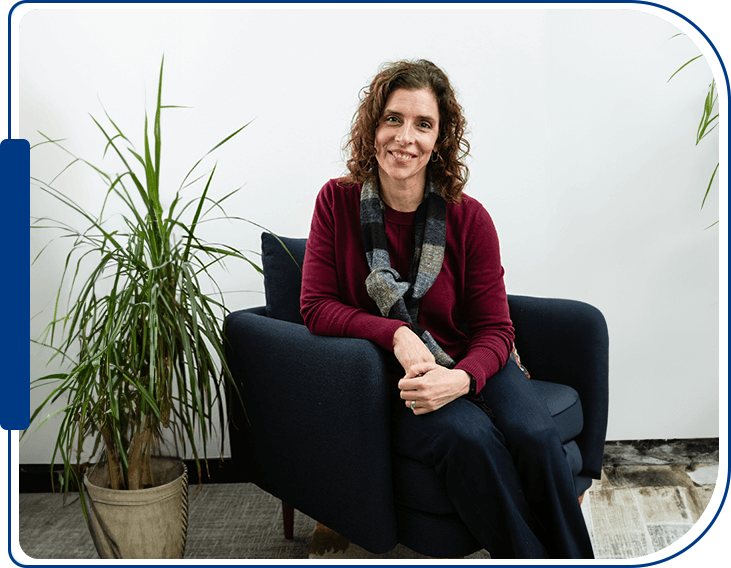 A woman sitting on top of a blue chair next to a plant.